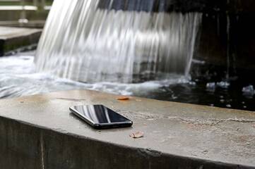 Smartphone liegt neben einem Brunnen auf einem Stein
