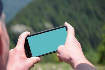 Person fotografiert eine bäumige Berglandschaft mit dem Smartphone