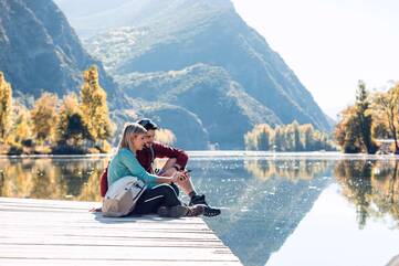 Mann und Frau sitzen auf Steg am See und schauen auf Smartphone
