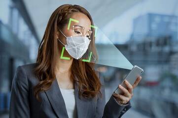 Frau hält Smartphone mit Gesichtsscanner vor ihr mit einem Mundschutz bedeckten Gesicht