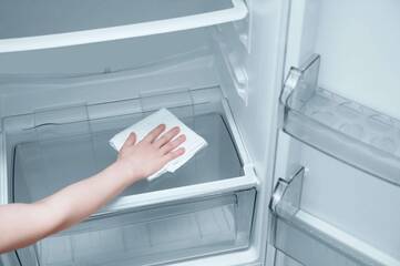 Jemand wischt mit einem weißen Tuch durch ein leeres Fach im Kühlschrank
