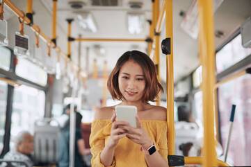 eine Frau steht im Bus und schaut auf ihr Smartphone