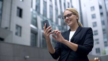 Frau in Business Kleidung schaut lächelnd auf Smartphone