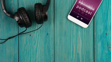 Smartphone mit Podcast Anzeige liegt neben Kopfhörerpaar