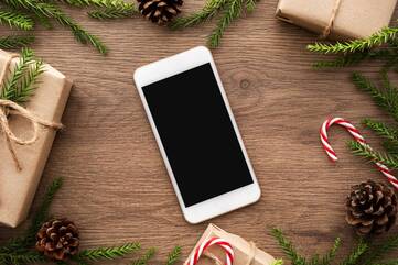 Smartphone liegt auf einem Tisch umgeben von Zuckestangen, Geschenken und Tannenzweigen
