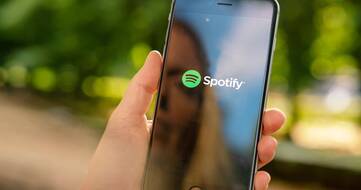 Frau hält iPhone 8 in der Hand, auf welchem Spotify startet