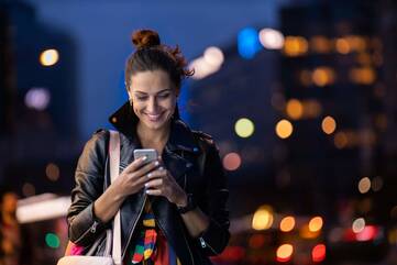 Frau in der Innenstadt schaut lächelnd auf ihr Smartphone