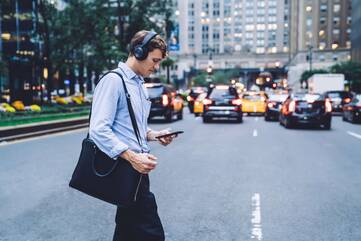 Mann mit Over-Ear-Kopfhörern und Smartphone in der Hand geht über die Straße