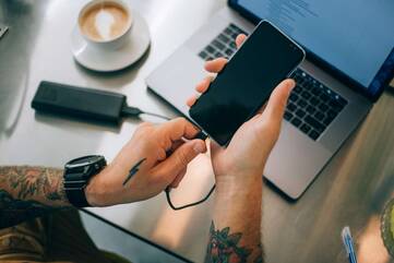 Hand steckt Ladekabel in Smartphone an Schreibtisch