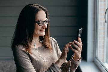 Frau schaut lächelnd auf Smartphone Display und bedient es mit der Hand
