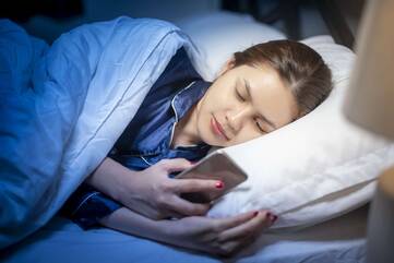 Person liegt im Bett mit Smartphone in der Hand
