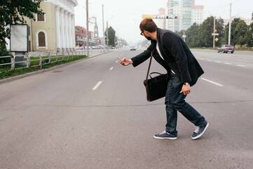 Mann läuft auf's Smartphone guckend über eine befahrene Straße