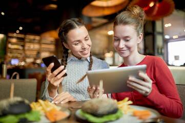Zwei Frauen mit Tablet und Smartphone im Restaurant