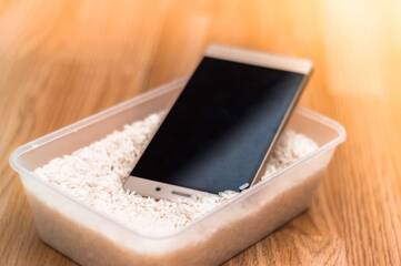 ein Smartphone liegt in einer Dose voller Reis
