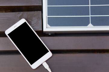 Smartphone mit Ladekabel neben Solarpanel