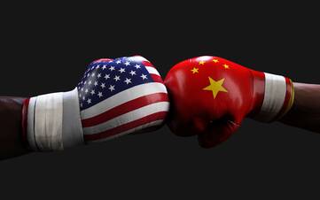 Zwei Boxhandschuher die aufeinander treffen, der linke im Desing der amerikanischen Flagge und der rechte im Design der chinesichen Flagge.