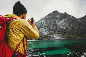 Mann in gelber Jacke fotografiert einen Berg mit dem Smartphone