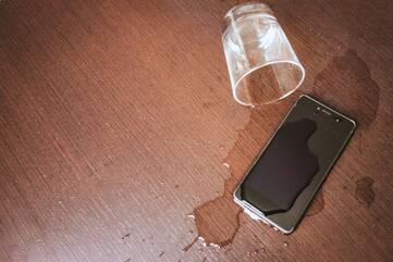 Smartphone mit Wasser aus einem umgekippten Glas übergossen