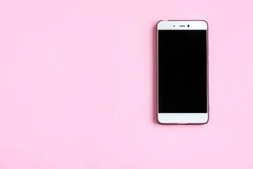 Weißes Smartphone liegt auf pinken Hintergrund