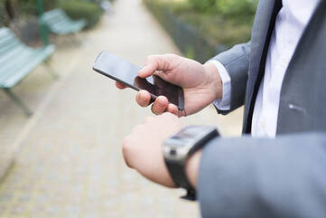 Businessman hält Smartphone in der rechten Hand. Checkt auf der linken die Uhrzeit auf seiner Armbanduhr