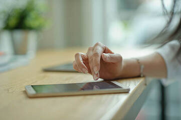 Weibliche Hand tippt auf ein Smartphones, welches auf einem Holztisch liegt,