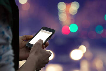 Handy wird vor einem Hintergrund voller unscharfer Lichtquellen bedient