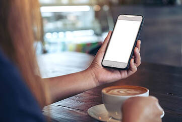 Smartphone wird in der Hand gehalten, daneben steht ein Kaffee.