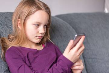 Mädchen sityt auf einem Sofa und hält ein Smartphone in der Hand