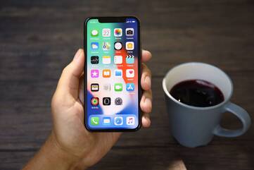 Hand hält ein entsperrtes iPhone der X-Reihe mit Kaffee im Hintergrund
