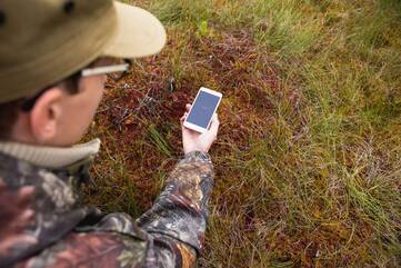 Mann in der Natur guckt auf eine Kompass-App auf seinem Smartphone