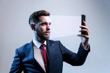 Mann im Anzug hält sein Smartphone auf Kopfhöhe vor sein Gesicht