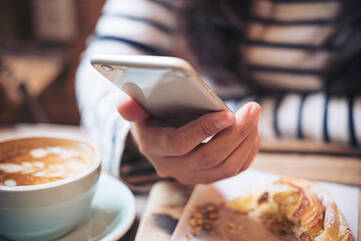 Eine Frau hält ein weißes Smartphone beim Frühstück