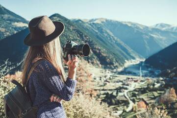 Frau guckt mit einer Digital-Kamera in der Hand über ein Tal
