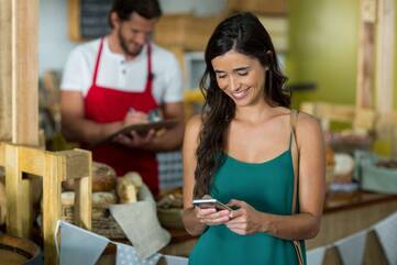 Frau in Bäckeri schaut lächelnd auf ihr Smartphone