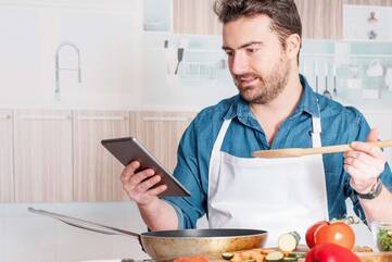 Kochender Mann schaut auf Smartphone Display