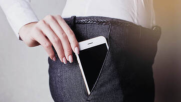 Frau steckt weißes Smartphone in die Hosentasche