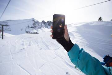 Person hält schwarzes Smartphone im Skigebiet