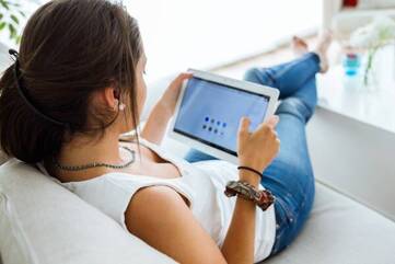 Frau sitzt auf dem Sofa und hält Lenovo Smart Tab in der Hand.
