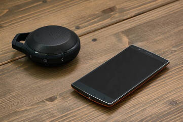 Smartphone liegt auf Tisch neben einem kleinen Bluetooth-Lautsprecher