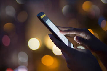 Hände bedienen Smartphone vor lichternem Hintergrund