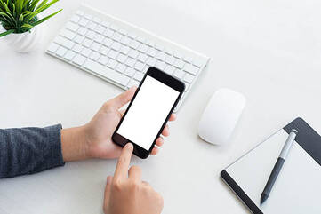 Hände bedienen ein Smartphone vor einem weißen Schreibtisch