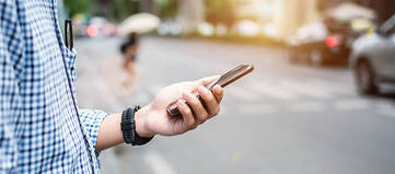 Mann hält Smartphone in einer Hand vor einer Straße