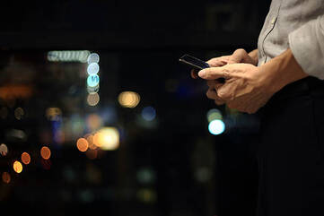 Mann hält Smartphone auf Schritthöhe vor dunklem Hintergrund