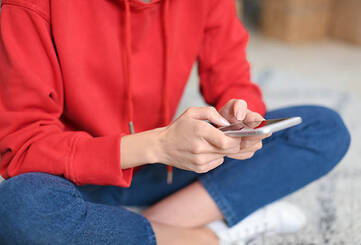Mensch in rotem Pullover bedient Smartphone mit beiden Händen
