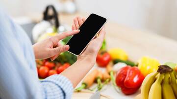 Person tippt auf Smartphone vor Obst und Gemüse im Hintergrund