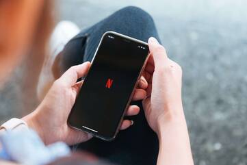 Person hält Smartphone mit Netflix-Symbol in der Hand