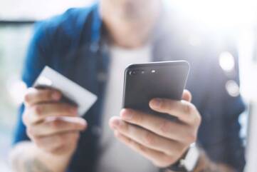 Mann hält sein iPhone in der einen und seine Kreditkarte in der anderen Hand