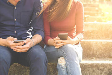 Pärchen sitzt auf Steintreppen mit Smartphones in den Händen