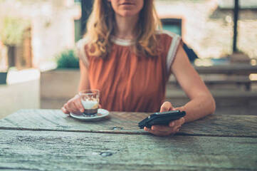Frau sitzt draußen am Tisch mit Kaffee und Smartphone