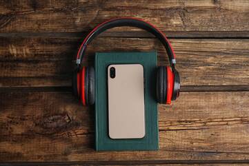 iPhone liegt auf einem grünen Buch, welchem Kopfhörer aufgesetzt wurden